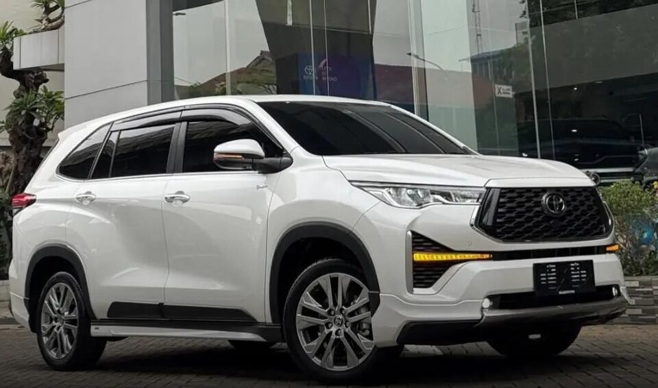 White Toyota SUV parked outside a modern glass-front dealership with the Toyota logo above it.