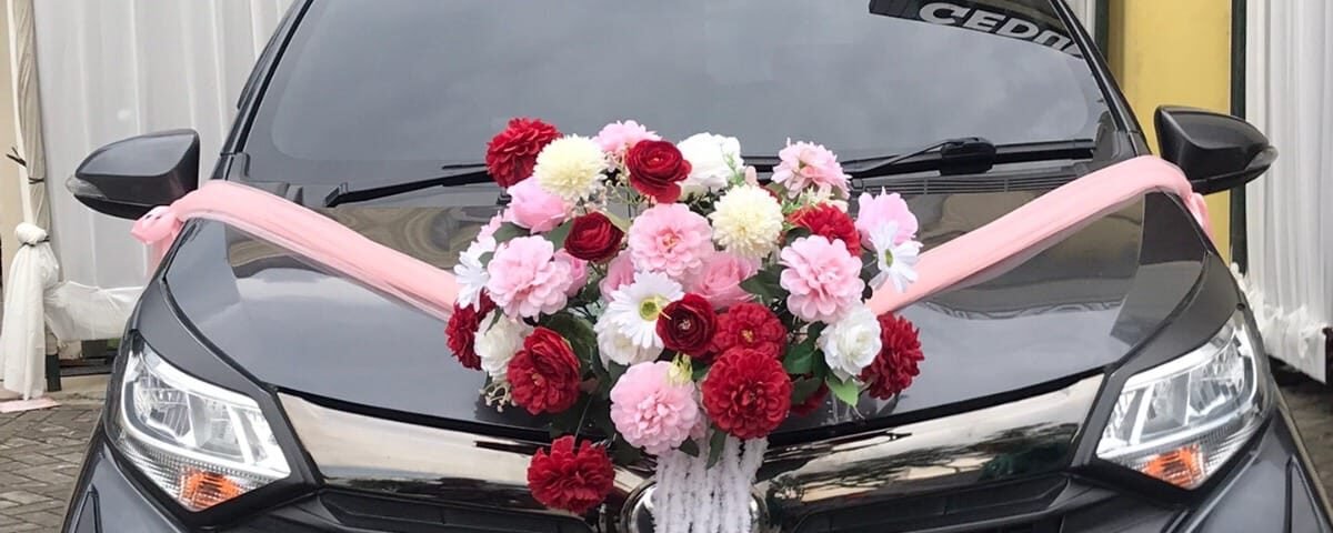 Black wedding car with pink ribbon and a large floral centerpiece (pink, white, red flowers) on the hood.