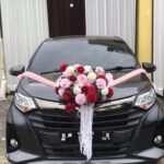 Black wedding car with pink ribbon and a large floral centerpiece (pink, white, red flowers) on the hood.