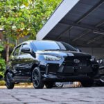 Front three-quarter view of a shiny black Toyota SUV parked on a paved area near a metal carport with green trees in the background