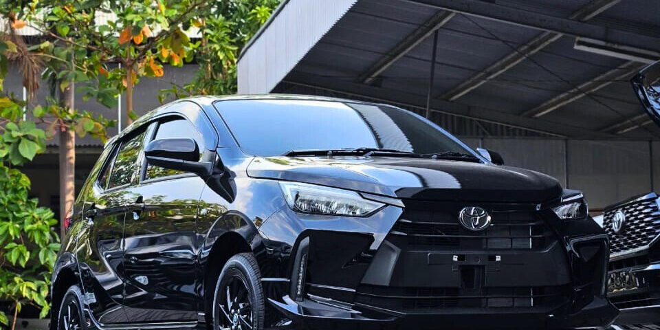 Front three-quarter view of a shiny black Toyota SUV parked on a paved area near a metal carport with green trees in the background