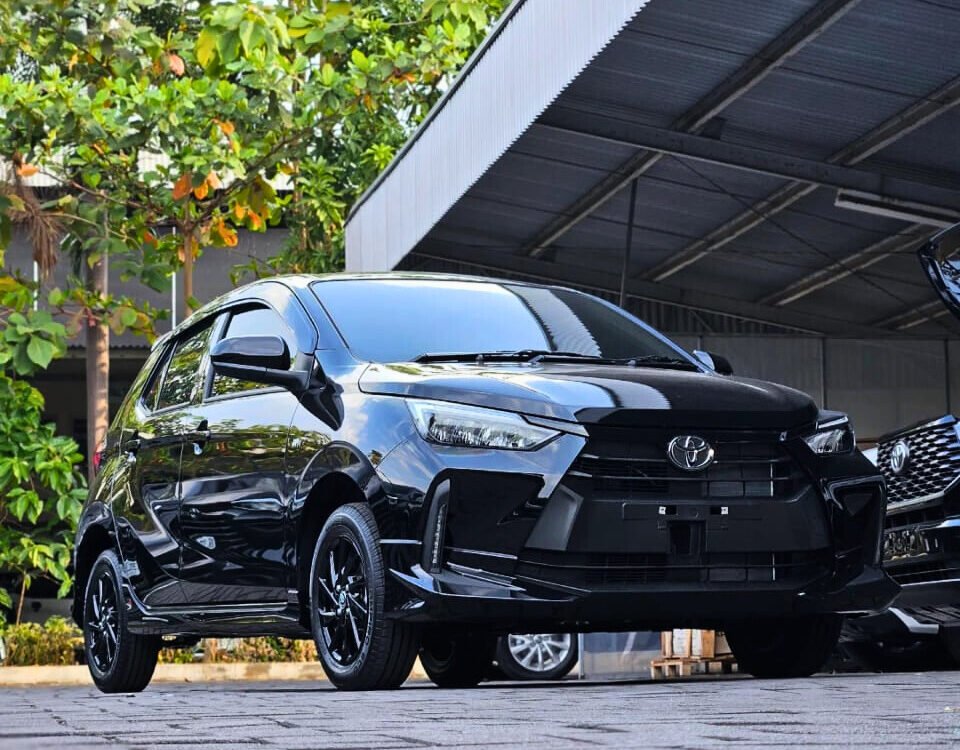Front three-quarter view of a shiny black Toyota SUV parked on a paved area near a metal carport with green trees in the background