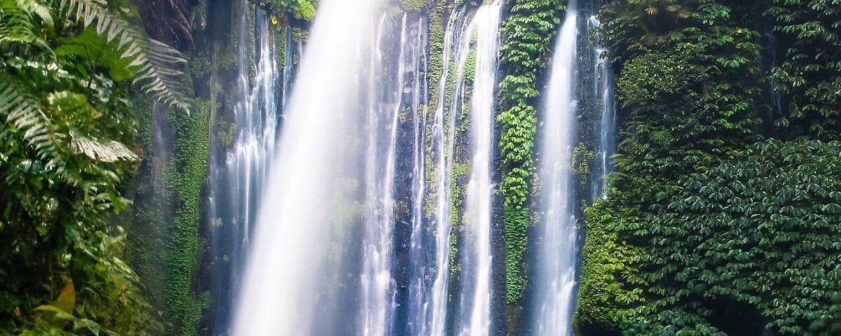 Waterfall pouring over a lush, mossy cliff into a rocky pool, surrounded by dense tropical jungle greenery