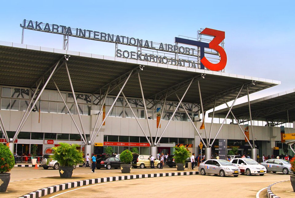 Exterior of Jakarta International Airport Terminal 3 (Soekarno–Hatta), with a large red 3 sign and cars dropping off under a glass-front façade.