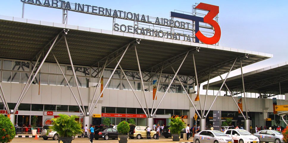 Exterior of Jakarta International Airport Terminal 3 (Soekarno–Hatta), with a large red 3 sign and cars dropping off under a glass-front façade.