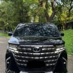 alphard canvas 1 - Dyantransport Front view of a black Toyota SUV with a large chrome grille parked on a tree-lined road.