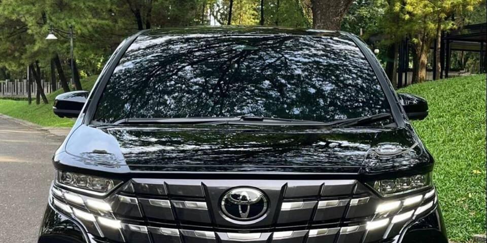 Front view of a black Toyota SUV with a large chrome grille parked on a tree-lined road.