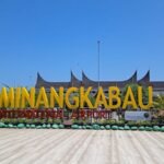 Large yellow MINANGKABAU sign for Minangkabau International Airport with a tiled forecourt and green decorative plants.