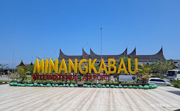 Large yellow MINANGKABAU sign for Minangkabau International Airport with a tiled forecourt and green decorative plants.