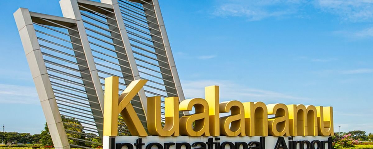 Kualanamu International Airport sign with large yellow letters and modern metal arches against a blue sky—Del Serdang, Indonesia (front view).