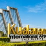 Kualanamu International Airport sign with large yellow letters and modern metal arches against a blue sky—Del Serdang, Indonesia (front view).