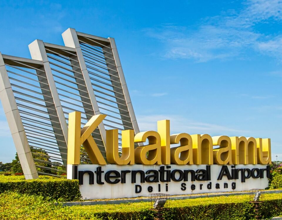 Kualanamu International Airport sign with large yellow letters and modern metal arches against a blue sky—Del Serdang, Indonesia (front view).