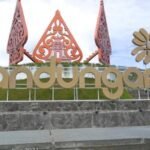 Large outdoor sign reading 'bandungan' with decorative red carved structures and a gold flower icon on a stone platform, outdoors.