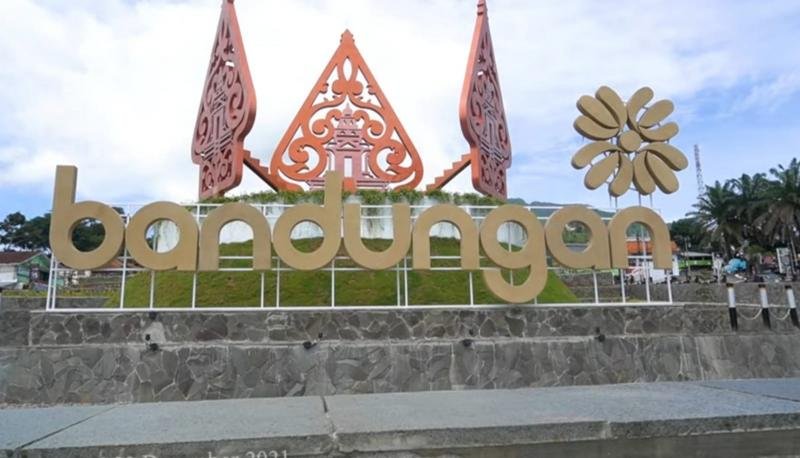 Large outdoor sign reading 'bandungan' with decorative red carved structures and a gold flower icon on a stone platform, outdoors.