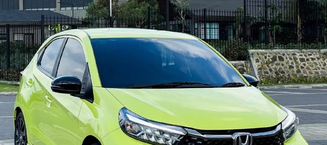 Lime green Honda BRIO RS parked on a paved lot with modern buildings in the background.