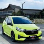 Lime green Honda BRIO RS parked on a paved lot with modern buildings in the background.