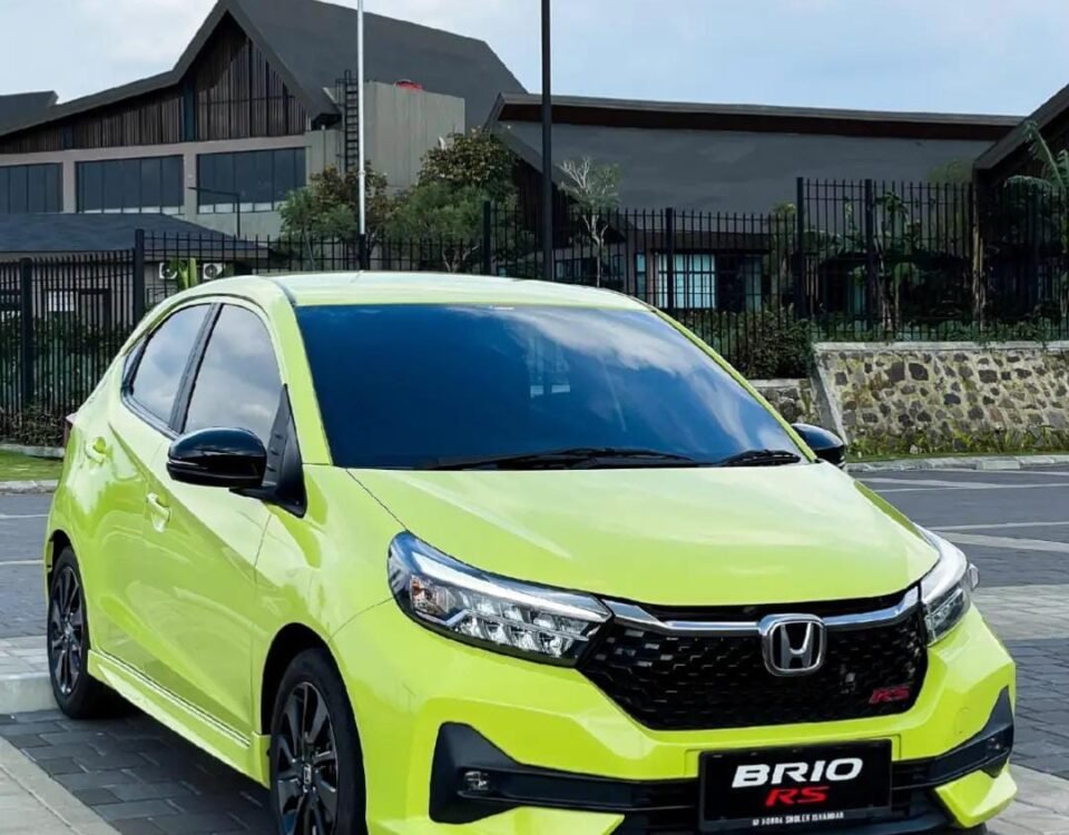 Lime green Honda BRIO RS parked on a paved lot with modern buildings in the background.