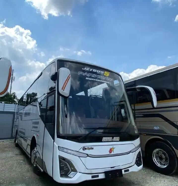 bus - Dyantransport Front three-quarter view of a white tour bus with a large windshield, parked on a gravel lot beside another bus under a cloudy blue sky.