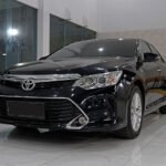 Front three-quarter view of a black Toyota sedan in a bright showroom, showing chrome grille and sleek headlights.