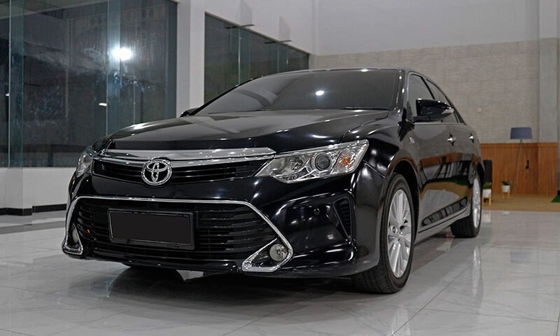Front three-quarter view of a black Toyota sedan in a bright showroom, showing chrome grille and sleek headlights.