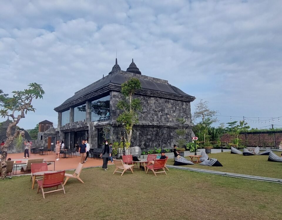 Stone pavilion and historic stone building on a grassy terrace with outdoor seating and string lights, visitors walking around.