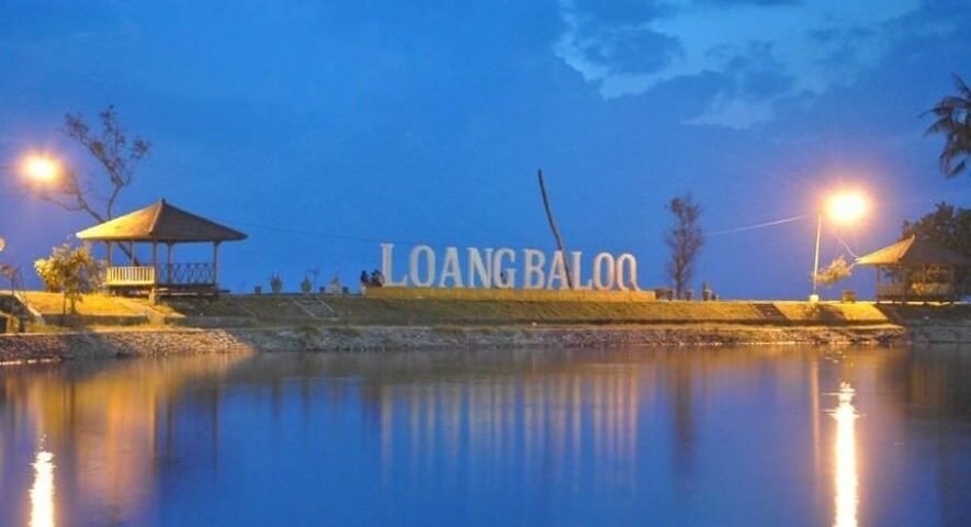 Lakeside park at dusk with a large sign reading 'LOANG BALOO', illuminated by street lamps and flanked by two gazebos overlooking calm water.