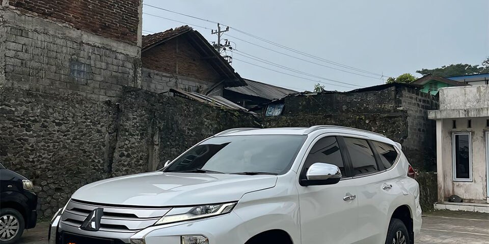 White SUV parked on a paved lot with brick buildings in the background; orange Dyan Transport logo on the front bumper area.