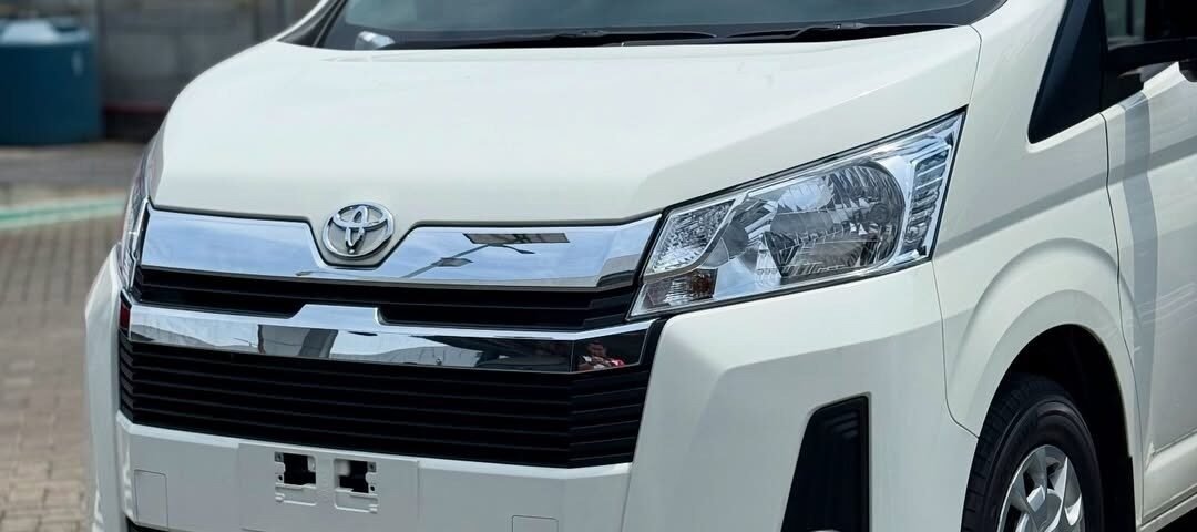 Front three-quarter view of a white Toyota van parked on a brick-paved lot, showing chrome grille and headlamps.