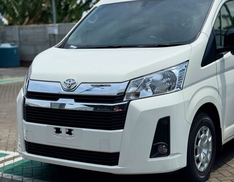 Front three-quarter view of a white Toyota van parked on a brick-paved lot, showing chrome grille and headlamps.