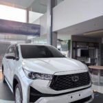 White Toyota SUV on display in a modern showroom, featuring a bold black grille and the orange DYAN TRANSPORT logo on the bumper.