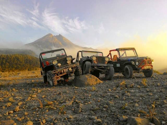 Three off-road jeeps parked on a rocky hillside with a distant mountain at sunset.
