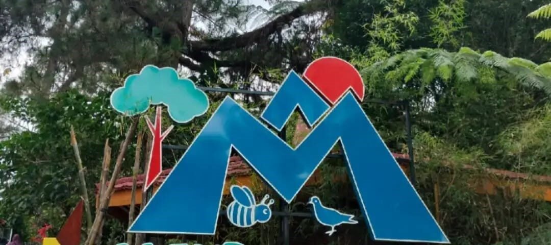 Sign for Kaliurang Park Botanical Garden with a blue mountain logo, red sun, tree, bee and bird illustrations
