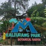 Sign for Kaliurang Park Botanical Garden with a blue mountain logo, red sun, tree, bee and bird illustrations