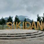 Large golden letters spelling 'SIKDANG' on a circular stone platform in an outdoor area with trees and distant mountains.