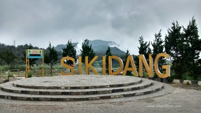 Large golden letters spelling 'SIKDANG' on a circular stone platform in an outdoor area with trees and distant mountains.