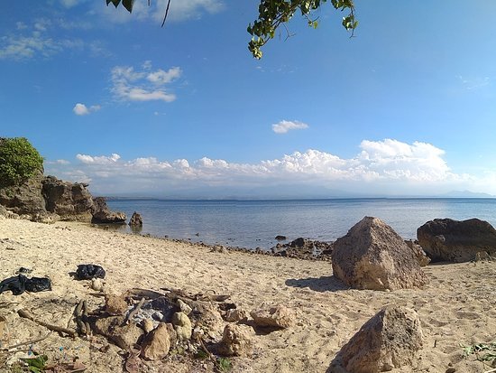 Calm sandy beach with large rocks near the shore and a clear blue sky above the calm sea.