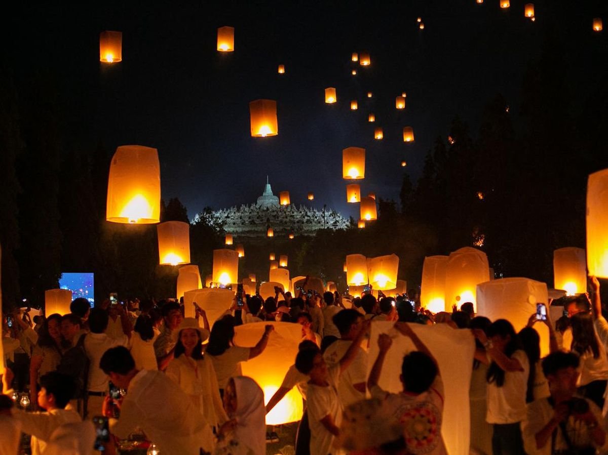 Crowd in white releases glowing orange sky lanterns at night during a lantern festival.