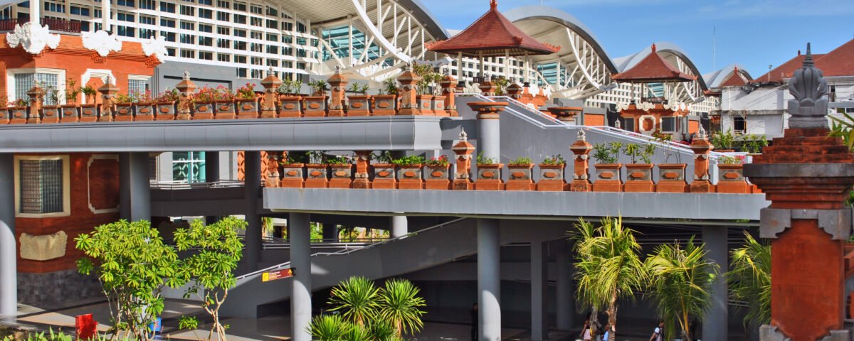 Wide view of a modern building with a large curved white roof, red brick walls, and decorative terraces under a blue sky.