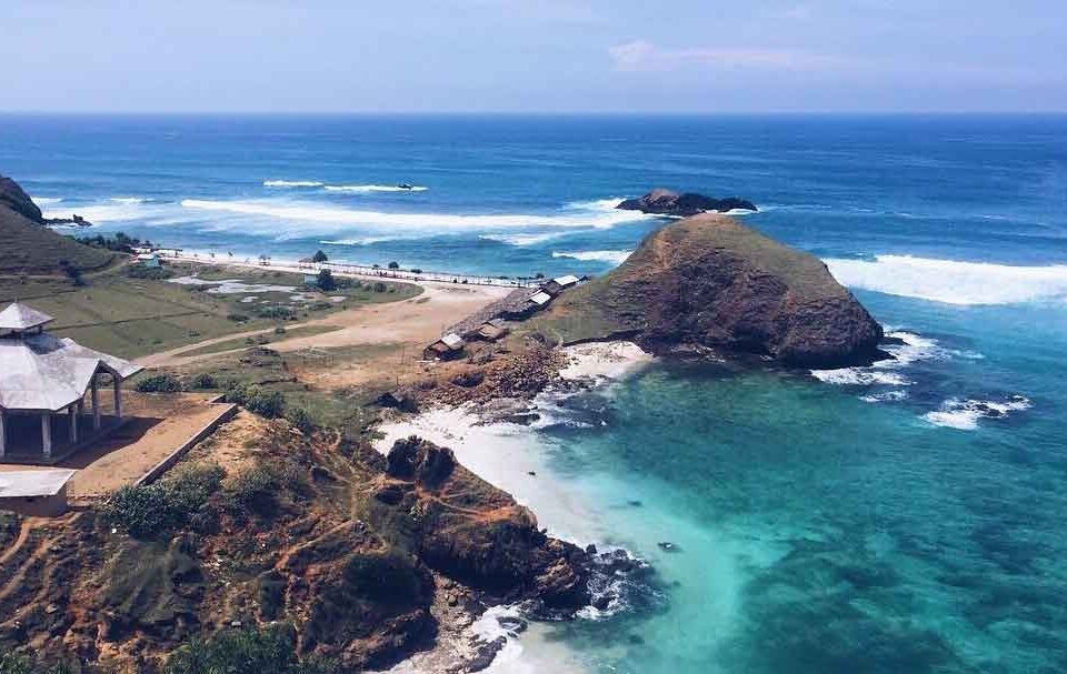 A coastal landscape with turquoise water, rocky promontory, and an open-air pavilion on the left overlooking the sea.
