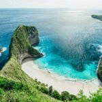 Cliffside cove with a white sand beach and turquoise water, surrounded by lush green cliffs overlooking the sea.