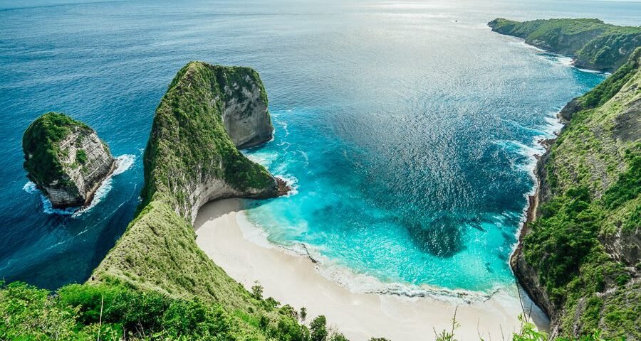 Cliffside cove with a white sand beach and turquoise water, surrounded by lush green cliffs overlooking the sea.