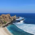 Cliffside coastline with white-sand beach and turquoise water meeting blue ocean under a clear sky