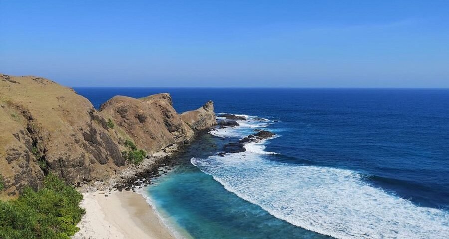 Cliffside coastline with white-sand beach and turquoise water meeting blue ocean under a clear sky