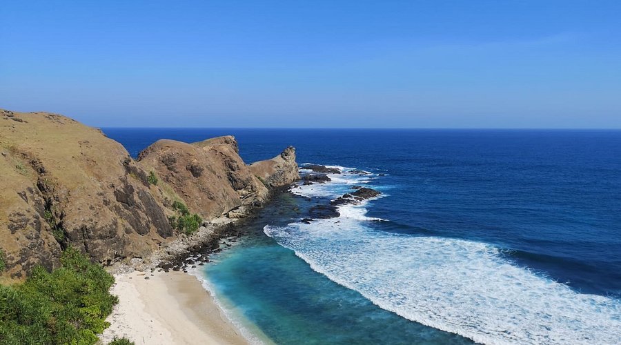 Cliffside coastline with white-sand beach and turquoise water meeting blue ocean under a clear sky