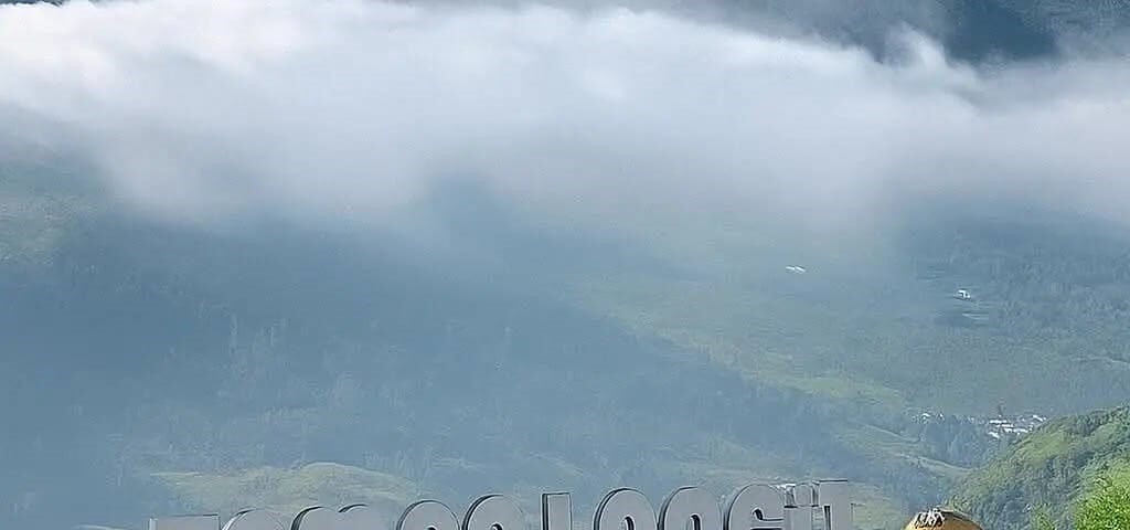 Mountain peak rising above clouds, with a scenic overlook featuring carved wooden goats and a Dieng sign in the foreground