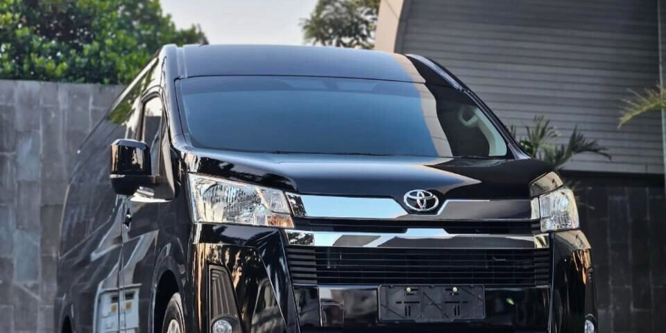 Front view of a black Toyota minivan parked on a paved surface near a modern building.