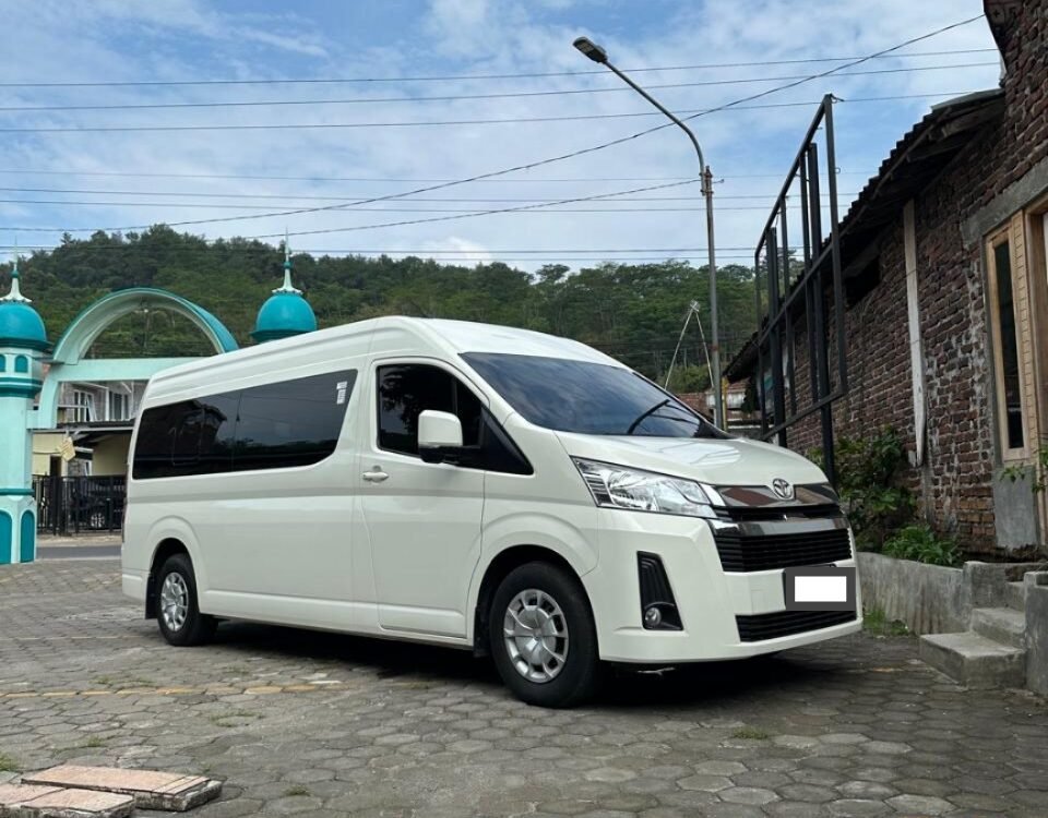 White Toyota van parked on a cobblestone lot beside a brick building, under a blue sky with clouds.