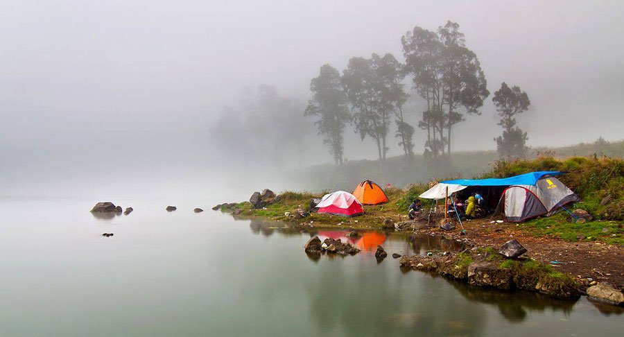 Misty lakeside campsite with colorful tents on a rocky shore and calm water reflecting the scene