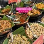 Assorted Indonesian dishes in clay bowls on banana leaves, with small labeled signs and spoons for serving, at a market stall