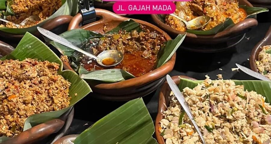Assorted Indonesian dishes in clay bowls on banana leaves, with small labeled signs and spoons for serving, at a market stall